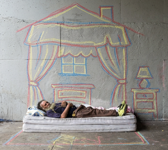 Chalk drawing of a house on a wall behind a person resting on a mattress